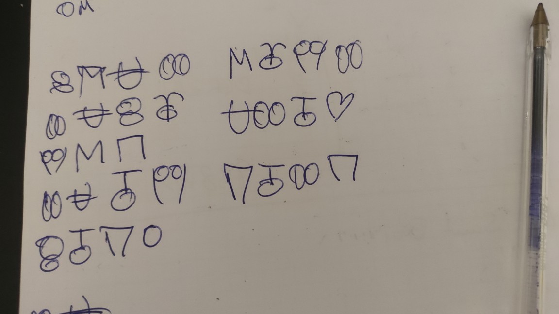 Fotografía de una hoja de papel con varias series de códigos y un bolígrafo a la derecha.